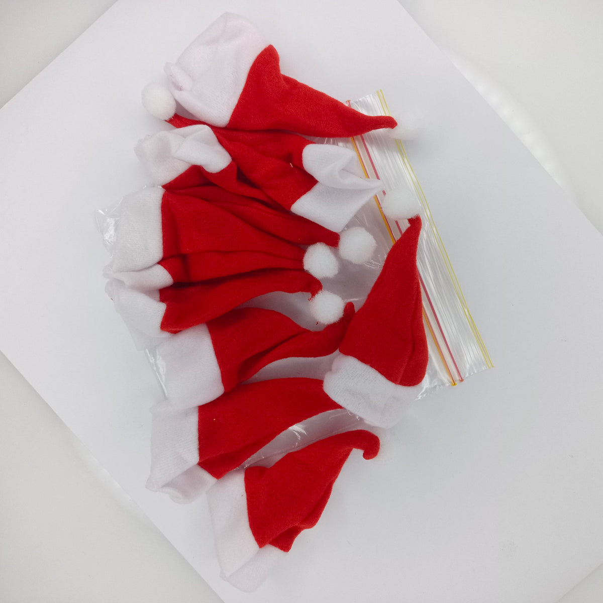 Miniature Santa Hats with Pom Poms 15cm – 9pcs – Several small red and white Santa hat felt pieces with white pom-poms, packaged in a clear plastic bag on a white background.
