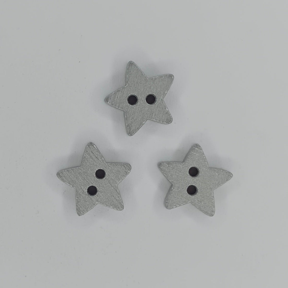 Star Wood Buttons 13mm 2 Holes – Silver & Gold – Three small gray wooden star-shaped buttons with two holes, arranged in a triangle on a plain white background.